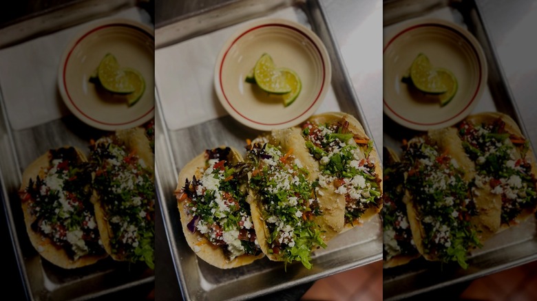 Three tacos on metal tray next to lime wedges