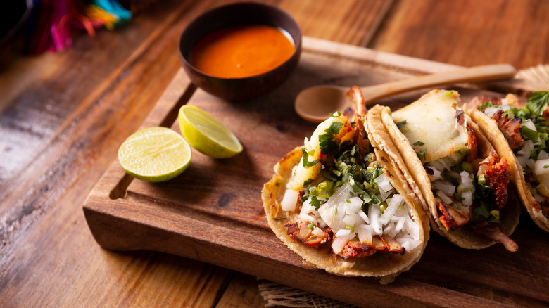 Three soft tacos on cutting board, cup of sauce behind