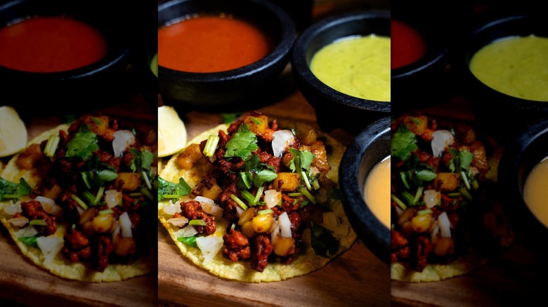 A close-up of an al pastor street taco on a counter surrounded by bowls of salsa