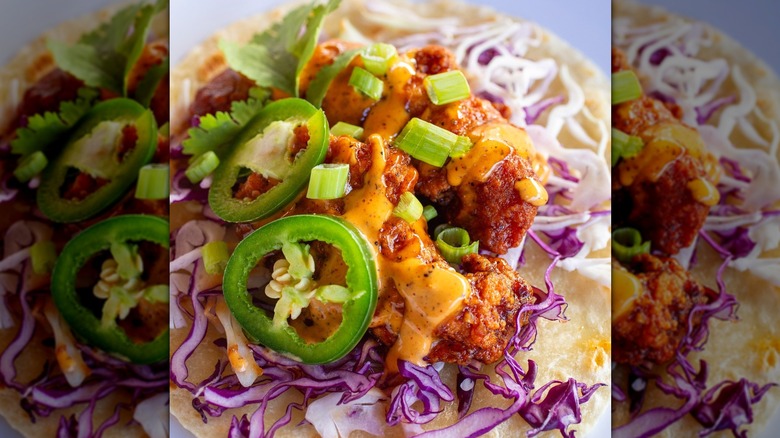 Close-up of fried chicken taco with jalapeño, green onions, red cabbage, sauce, cilantro