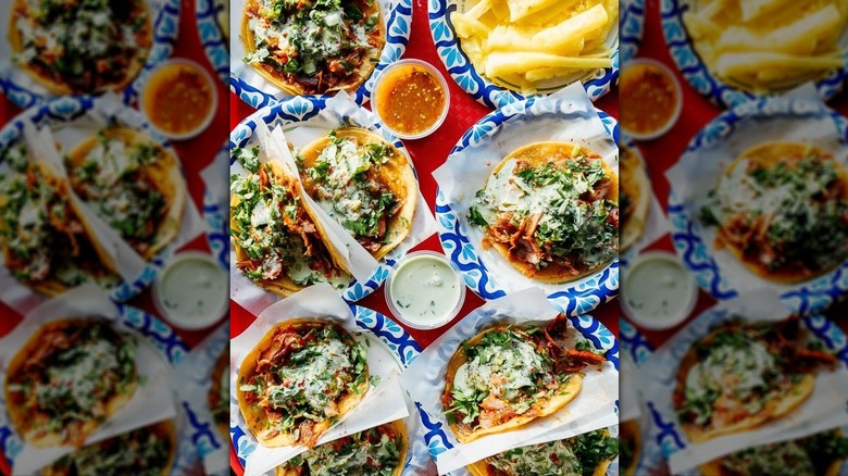 Overhead shot of multiple plates of soft tacos and cups of salsa on a red table