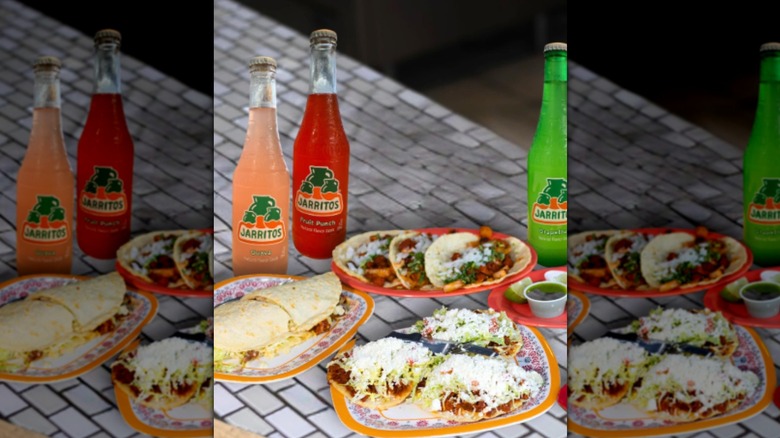 Three plates of loaded soft tacos on a table with bottles of Jarritos behind