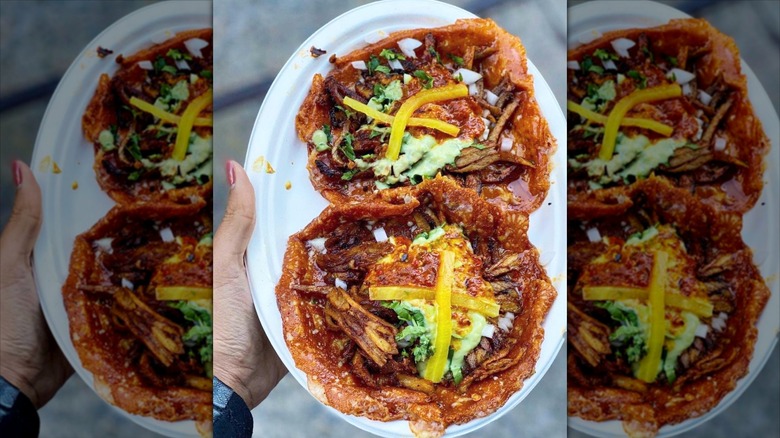 A hand holding a paper plate with two large tacos made with a fried cheese shell