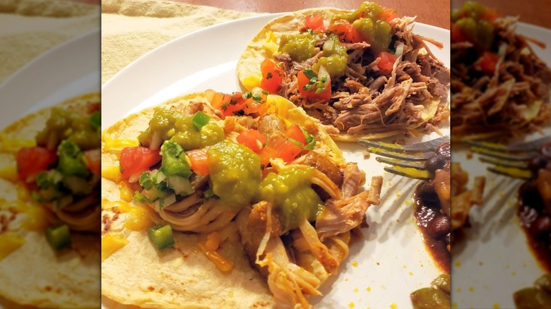 Close-up of pulled meat tacos with tomatoes and guacamole on white plate