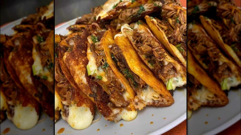Several fried soft tacos with pulled meat and melting cheese on white tray