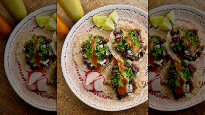 Overhead shot of three soft tacos on a pretty plate with lime wedges and radish slices