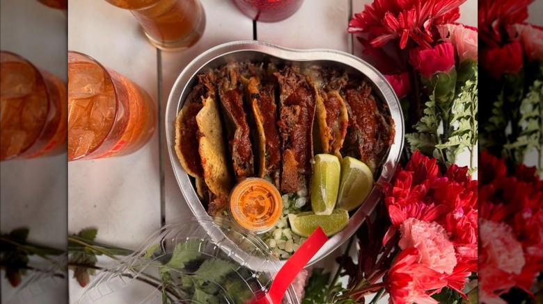 Overhead shot of a heart-shaped container filled with soft tacos, lime wedges and a sauce cup