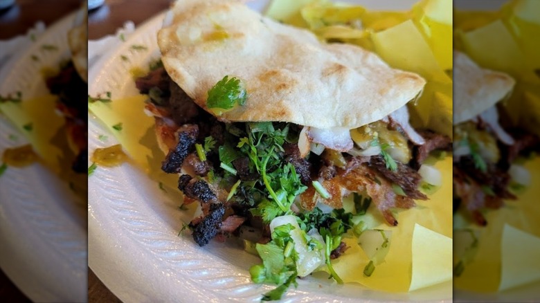A taco stuffed with charred meat and garnished with cilantro on a styrofoam plate with yellow paper
