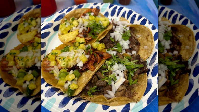 Four street tacos on a blue and white paper plate