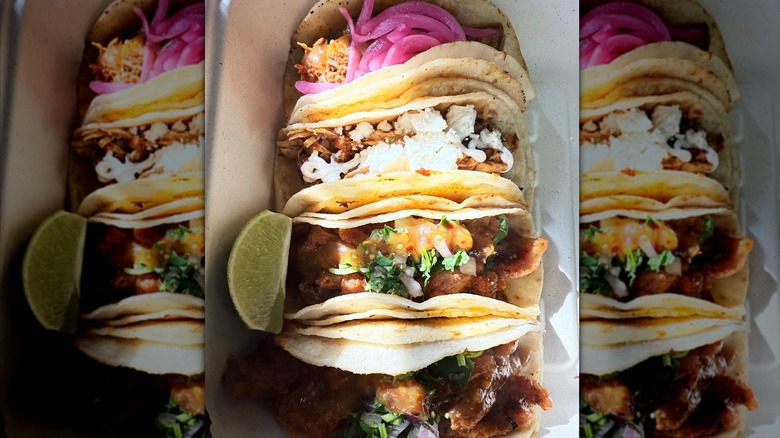 Close-up of four soft tacos in a container with a lime wedge beside