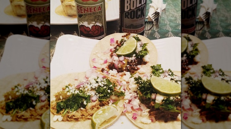 Three open soft tacos with lime wedges on white plate