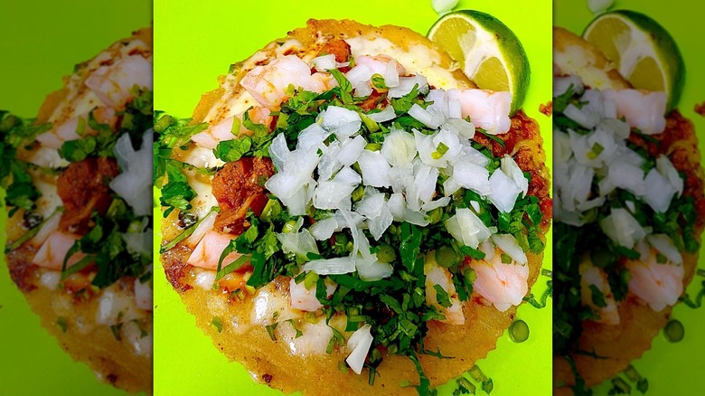 Close-up of a shrimp taco with cilantro, onions, lime wedge on bright green background