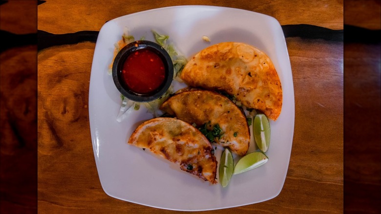 Overhead shot of three soft tacos, lime wedges, cup of salsa on white plate
