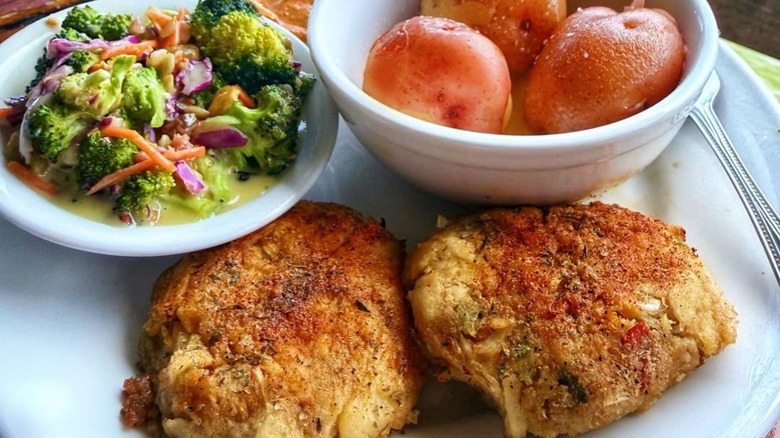 Two crab cakes on plate with sides of veg and potatoes