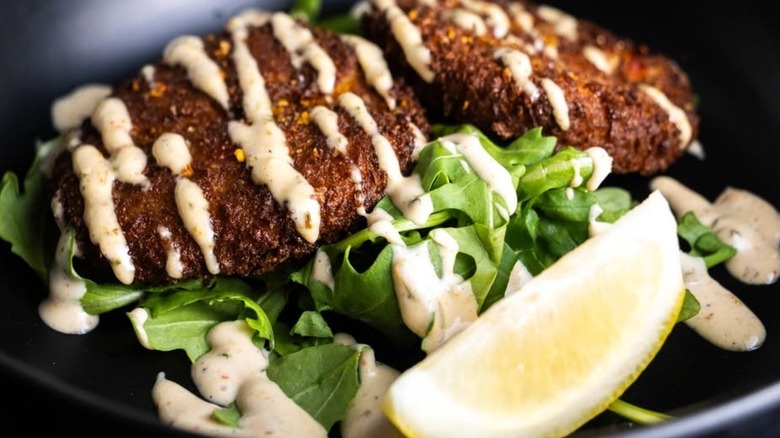 Two crab cakes with sauce and lemon on greens