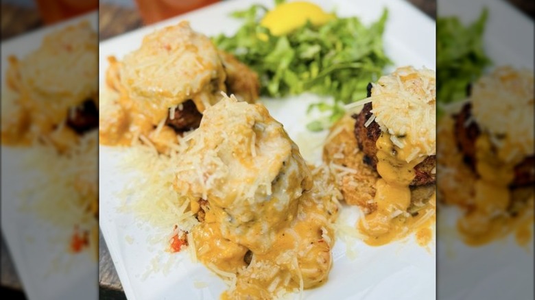 Dish of three crab cakes with sauce, cheese, and fried tomatoes