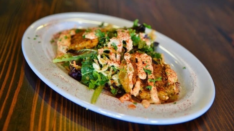 Crab cakes on plate with greens and drizzled sauce