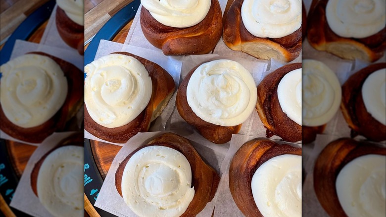 Seven frosted cinnamon rolls on individual squares of parchment paper