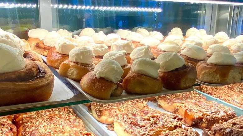 Dozens of frosted cinnamon rolls in pastry case above pecan sticky buns