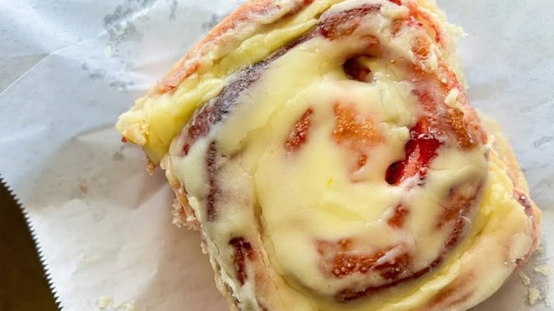 Cinnamon roll frosted in strawberry lemonade icing on parchment paper