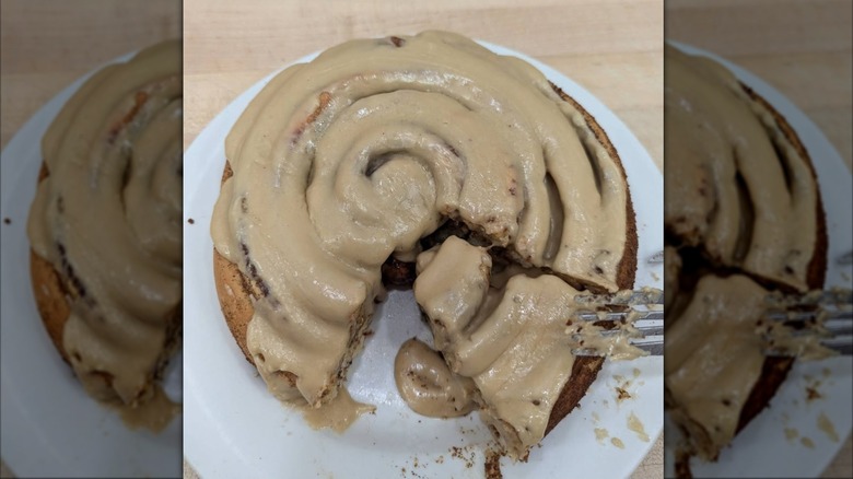Fork picking up a triangular slice of cinnamon roll from plate