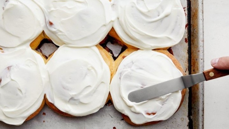 Hand using offset spatula to spread icing on cinnamon rolls