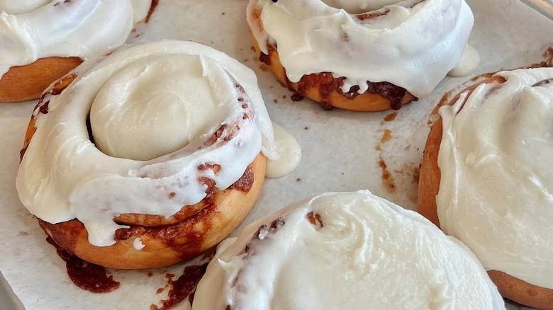 Several cinnamon rolls on baking sheet with caramelized sugar visible underneath frosting