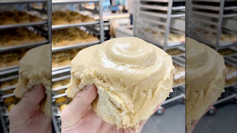 Hand holding fluffy, frosted cinnamon roll in bakery kitchen