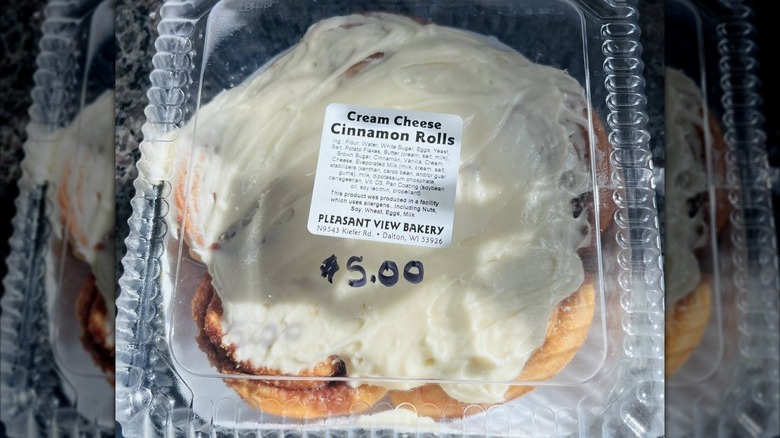 Cream cheese cinnamon roll in plastic take-out container with ingredient list sticker on top