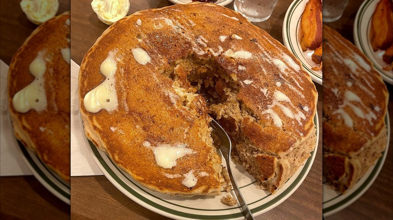 Top-down view of a fork slicing stack of pancakes on a white plate