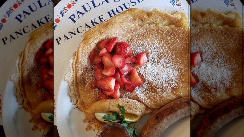 Stack of strawberry-topped pancaked and powdered sugar on white plate at Paula's Pancake House
