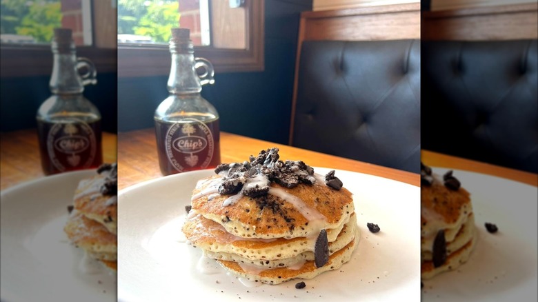 Stack of Oreo pancakes on white plate in front of syrup bottle
