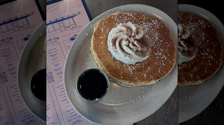 Top-down view of pancake stack with swirled whipped cream and side of maple syrup