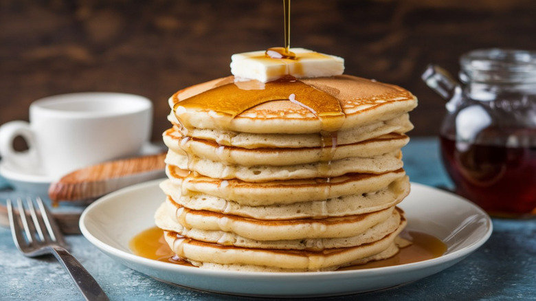 Stack of fluffy pancakes with pat of butter and drizzle of maple syrup