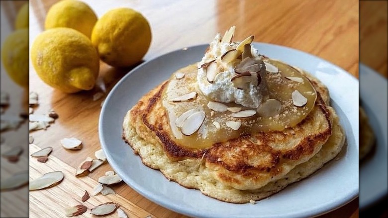 White plate with lemon curd pancakes topped with lemon curd, almond crumble, and whipped cream