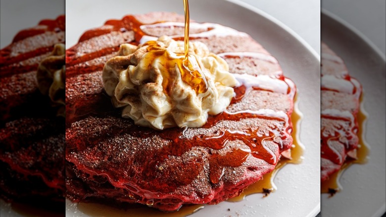 Syrup being poured onto red velved pancakes on white plate
