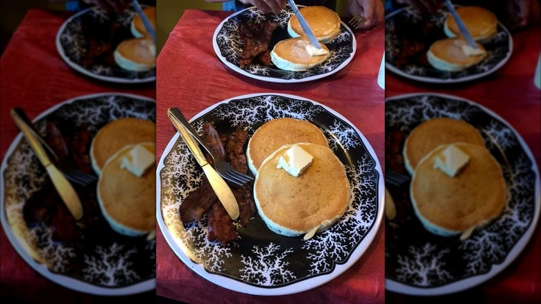 Pancakes with butter and bacon on black and white plate