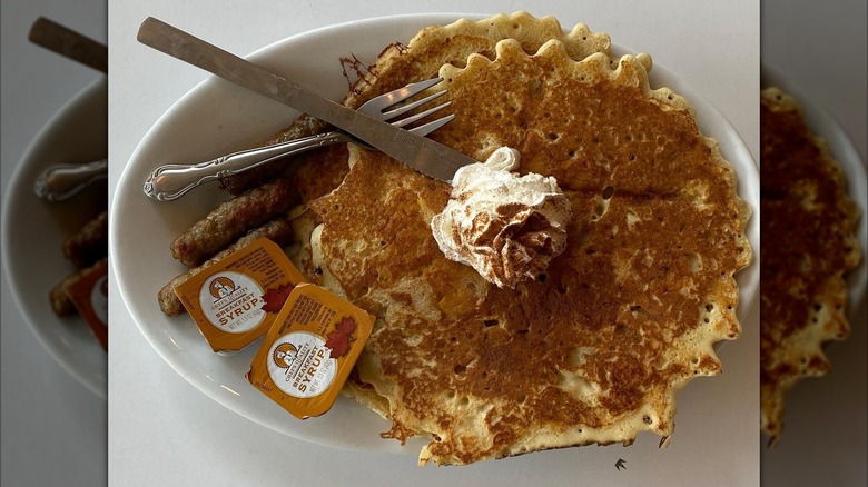 Two pancakes with maple syrup packets and sausage links on white plate