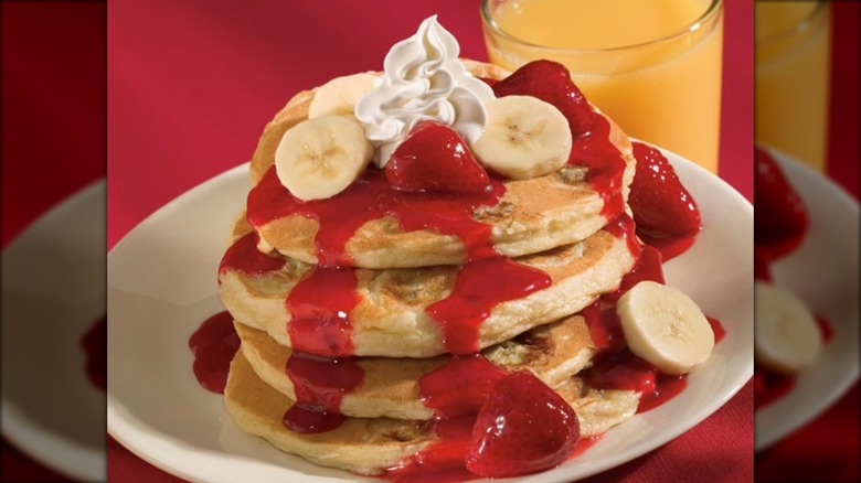 Stack of pancakes with strawberries and bananas on white plate