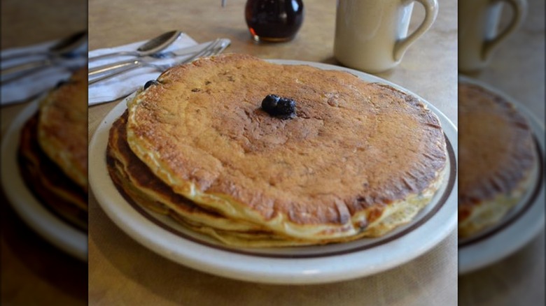 Stack of pancakes topped with two blueberries on white plate