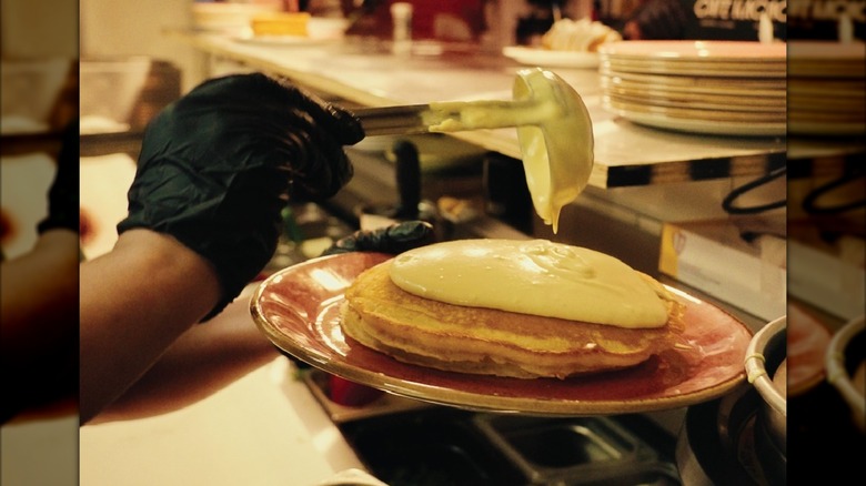 Hand ladling cream onto stack of pancakes on red plate