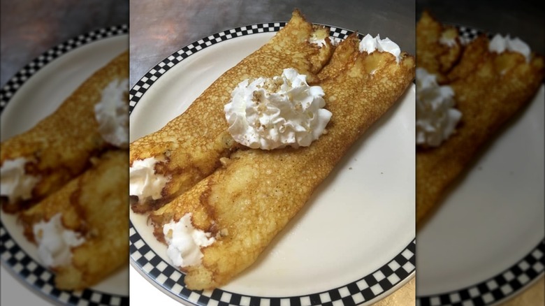 Cinnamon apple walnut hotcakes with whipped cream on white plate with checked border