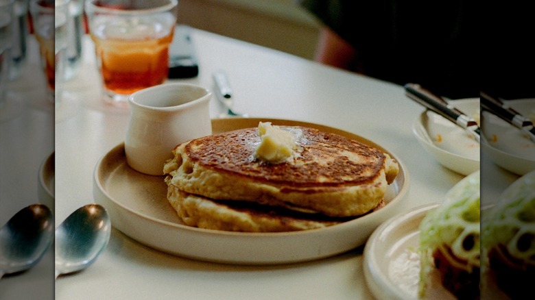 Two thick pancakes and butter next to pitcher of syrup on white plate