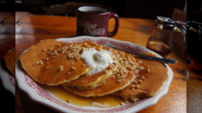 Four pancakes topped with butter, syrup, and nuts on red-rimmed white plate