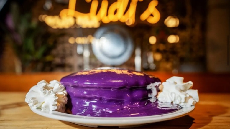 Stack of ube pancakes and two dollops of whipped cream on white plate