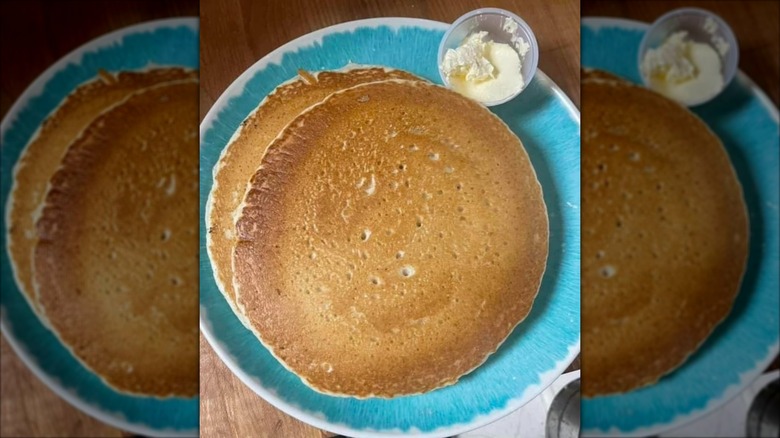 Top-down view of two pancakes on blue plate next to small cup of butter