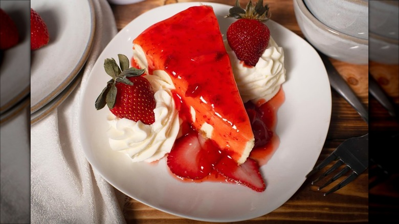 Top-down shot of strawberry sauce-covered cheesecake with whipped cream, strawberries on white plate