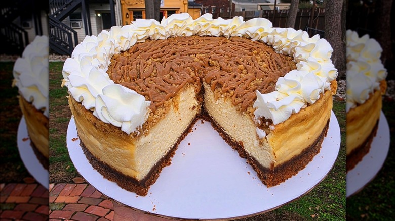 White plate holding whole cookie butter cheesecake with slice cut out of it