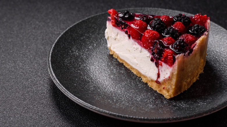 Slice of berry cheesecake topped with berries in gel on black plate