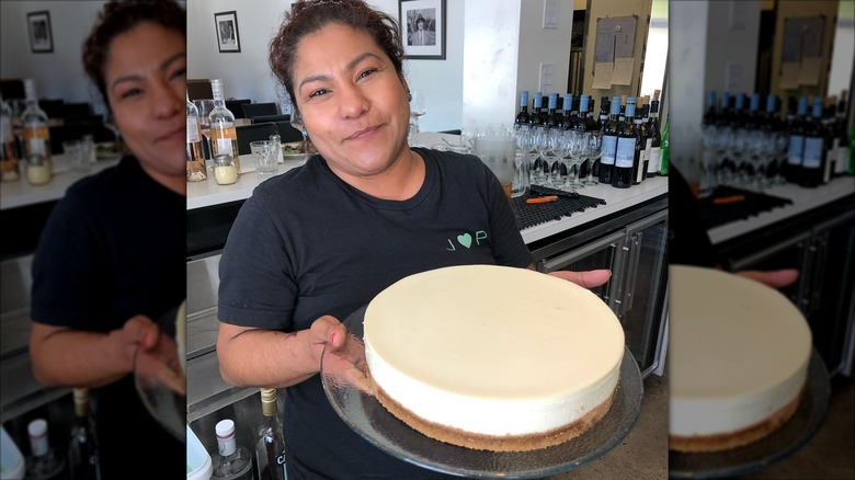 Woman holding whole plain cheesecake on glass platter